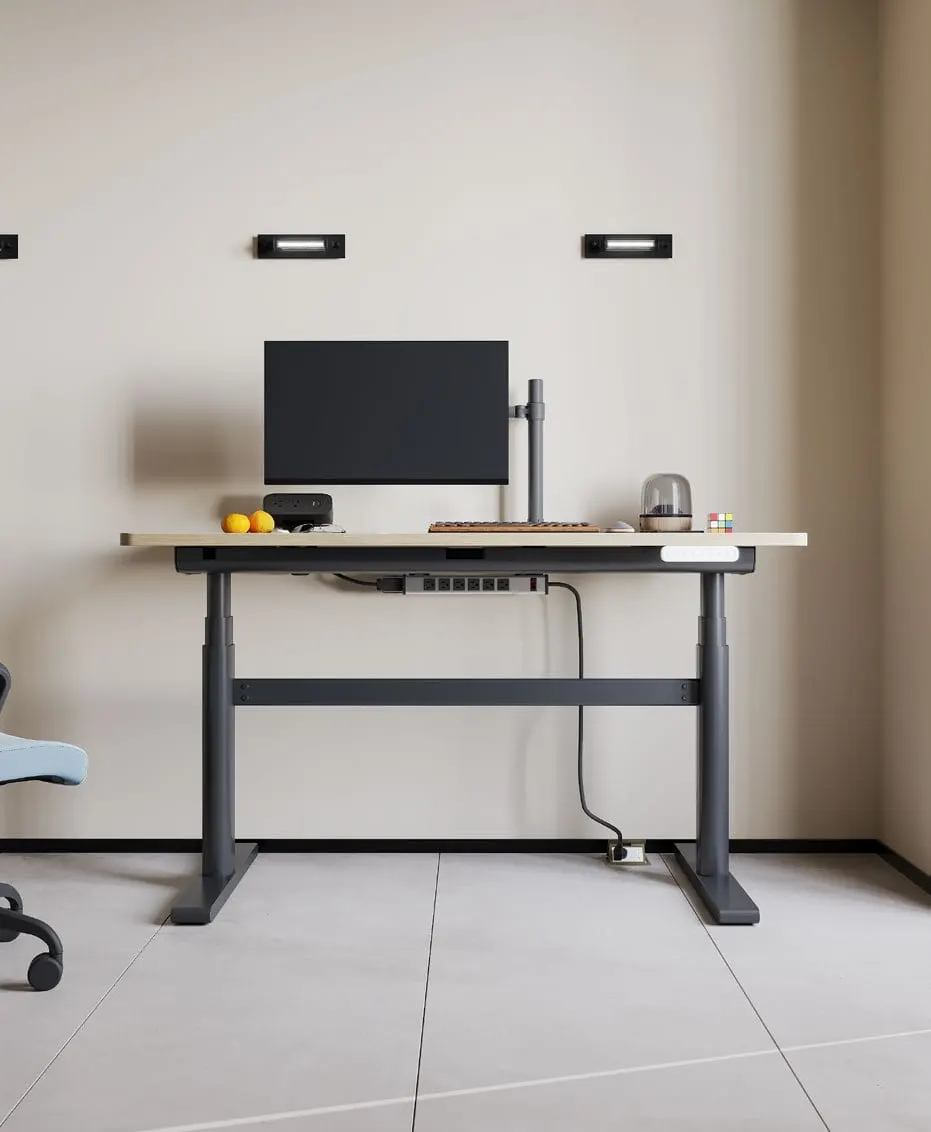 Graphite-frame height-adjustable desk with light wood top, monitor on pole arm and tidy under-desk cable tray
