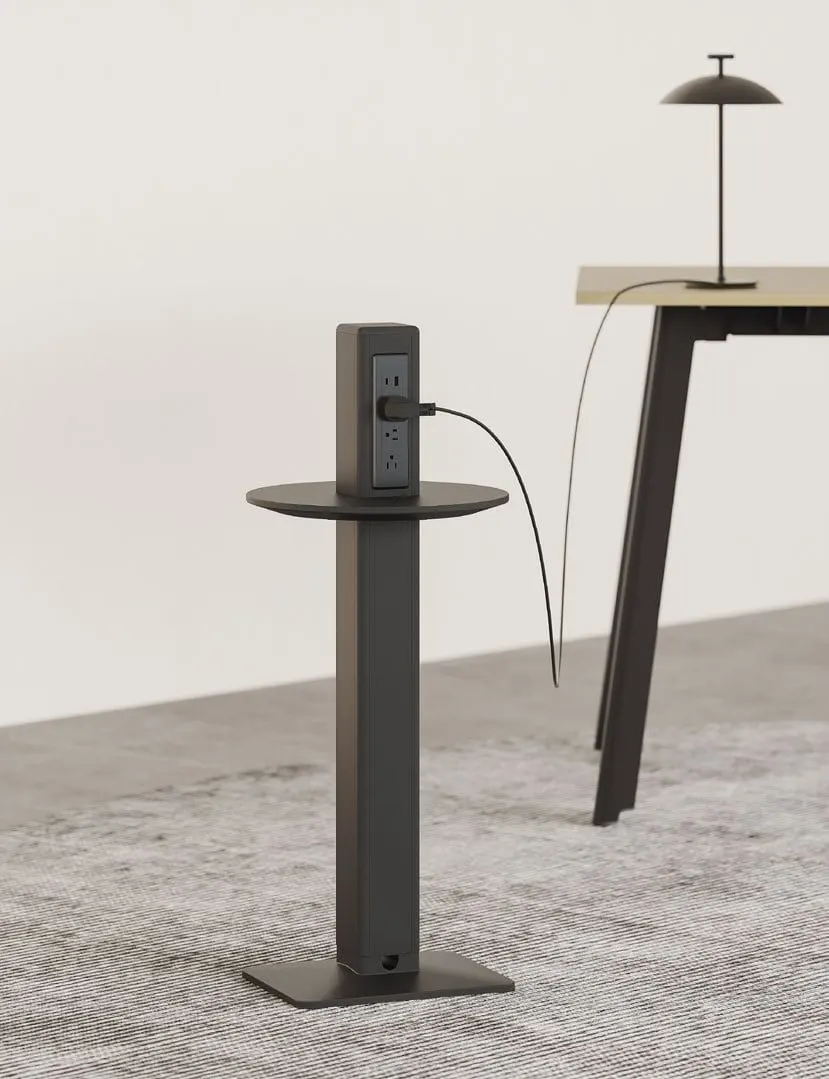 Black floor-standing power tower with round ledge and outlets charging a lamp beside a wooden desk
