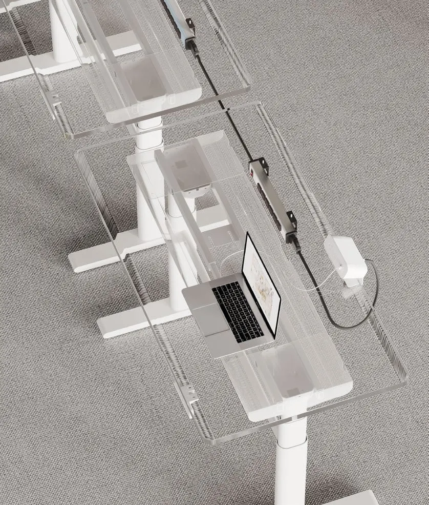 Transparent view of sit-stand desks showing an under-desk power rail feeding a clamp module and laptop charger