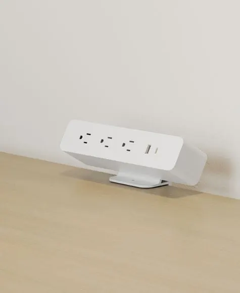 White desktop power module with outlets and USB port on a flat foot at an oak desk edge