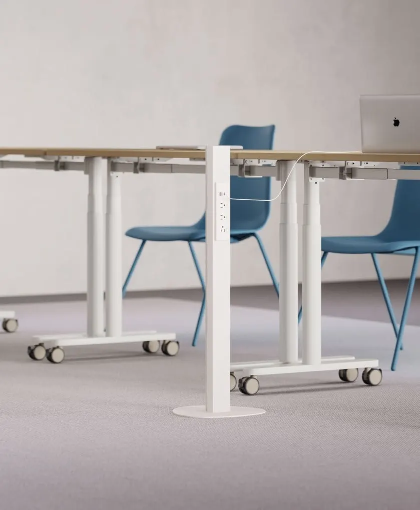 White floor-standing power pole with outlets beside mobile sit-stand tables and blue chairs on carpet